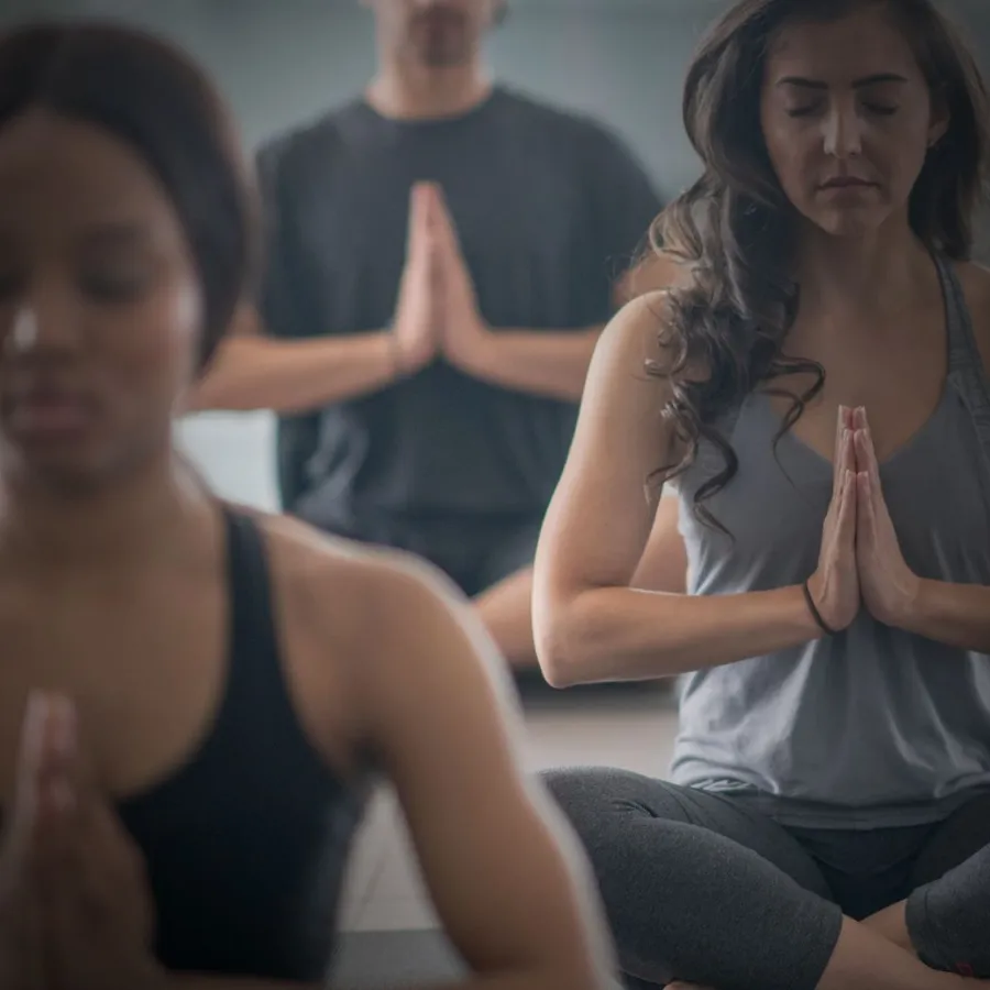 Students seated cross-legged with hands at heart center in a group class