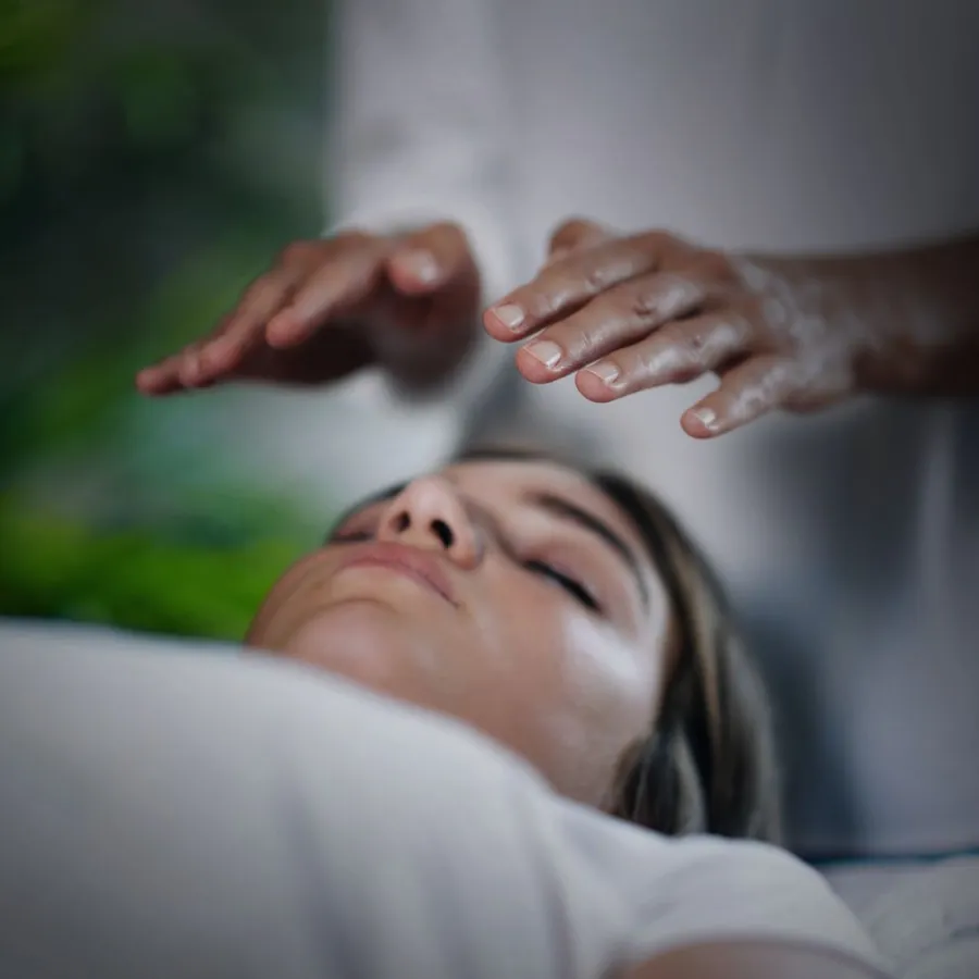 Practitioner holding hands above a resting client's head during a Reiki session